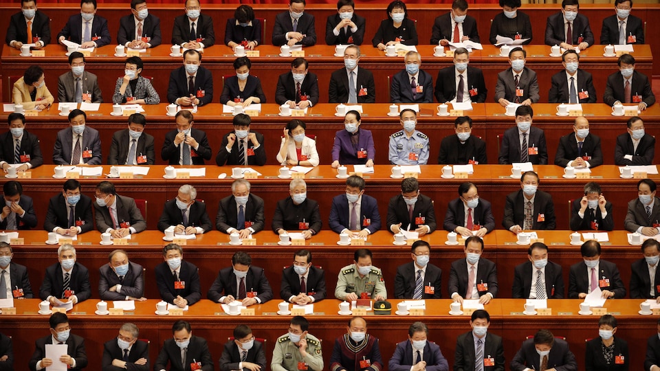 Des dizaines de Chinois, tous masqués, sont assis très près les uns des autres.