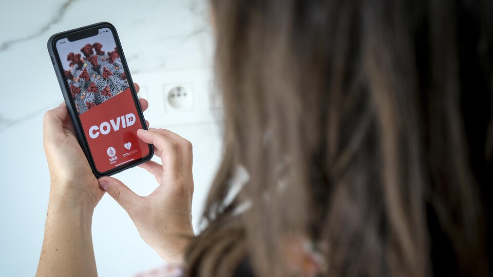 L'image du coronavirus apparaît sur l'écran d'un téléphone intelligent que tient dans ses mains une femme vue de dos.
