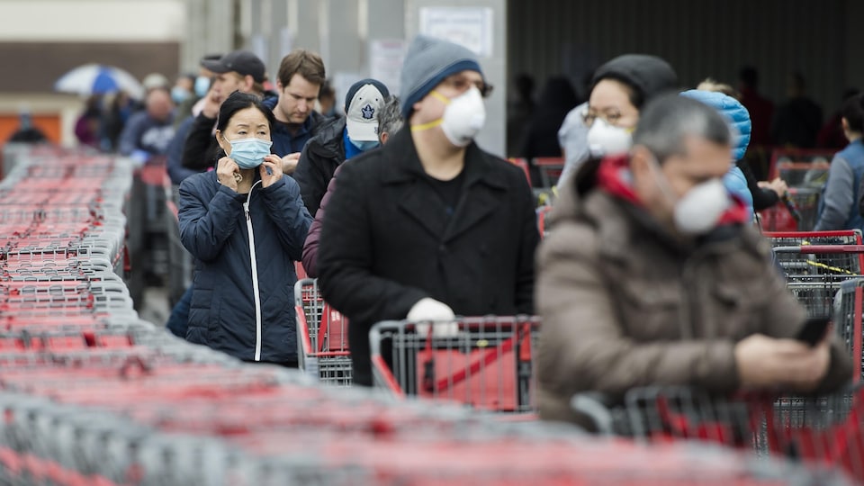 Une file de personnes portant un masque attendant avec leur panier d'épicerie.