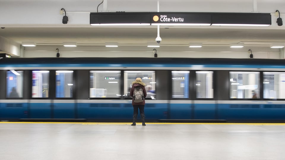 Une rame de métro de la ligne orange, déserte, vide. Seule une utilisatrice, de dos, attend de monter.