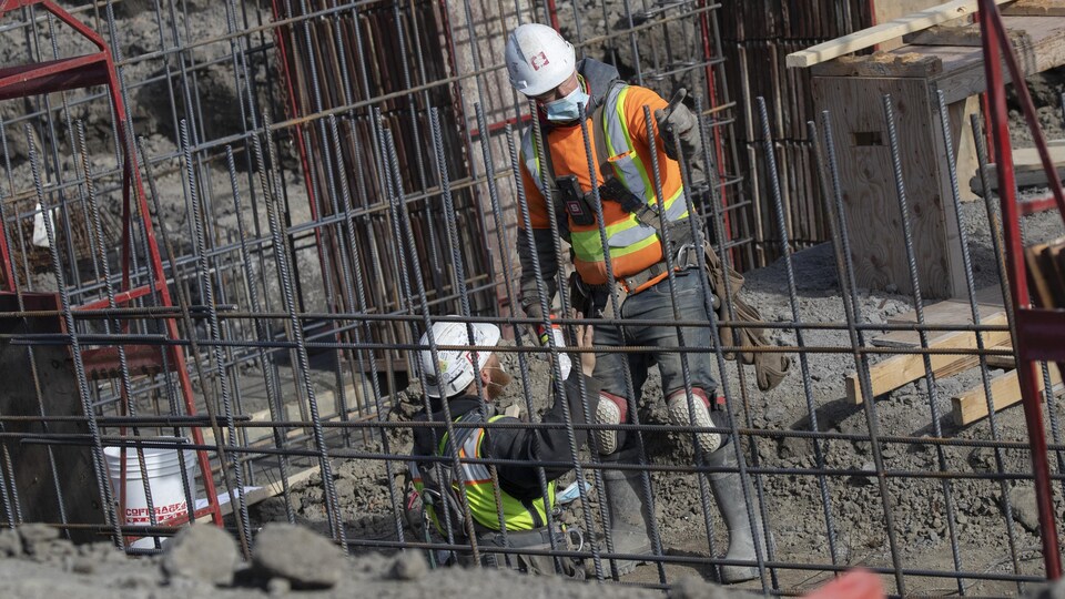 Deux hommes portant des masques se parlent sur un chantier de construction.