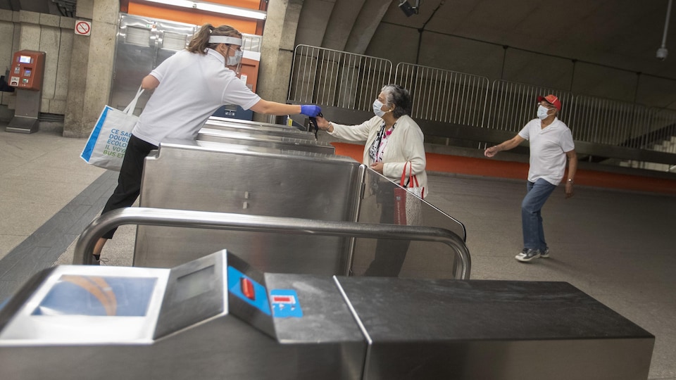 Une employée de la STM tend un masque à une dame dans la station de métro  Langelier.