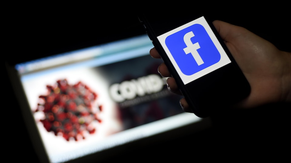 Un téléphone montrant le logo de Facebook est placé devant un écran d'ordinateur montrant une modélisation du coronavirus. 
