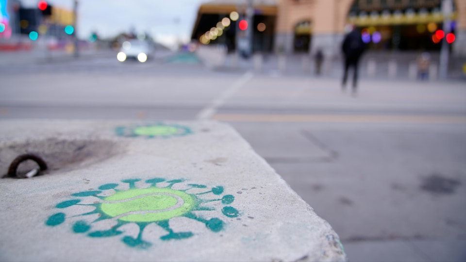 Dans une rue presque déserte, un graffiti sur un bloc de béton représente le coronavirus avec une balle de tennis au centre.