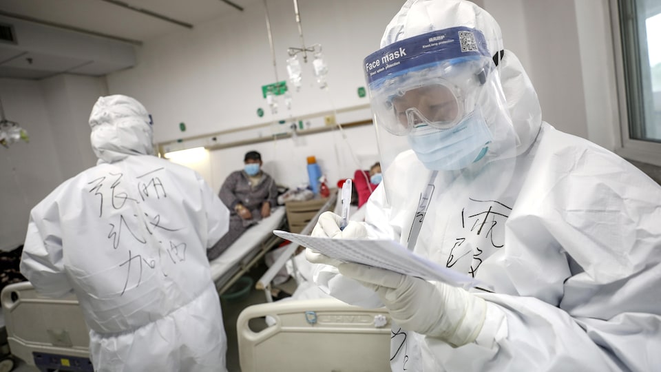 Deux employés dans un hôpital, vêtus de combinaison de protection, avec deux patients.