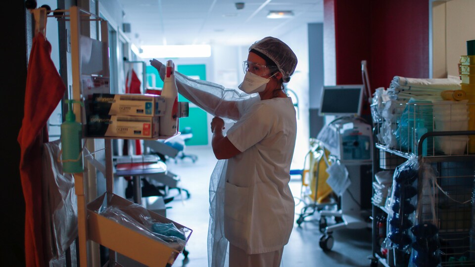Une infirmière enfile un uniforme de protection dans un corridor d'hôpital. 