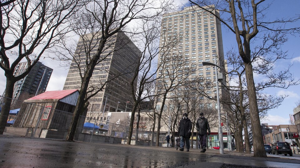 Deux personnes portant des masques marchent sur le trottoir en face de l'hôtel de la Place Dupuis au centre-ville de Montréal.