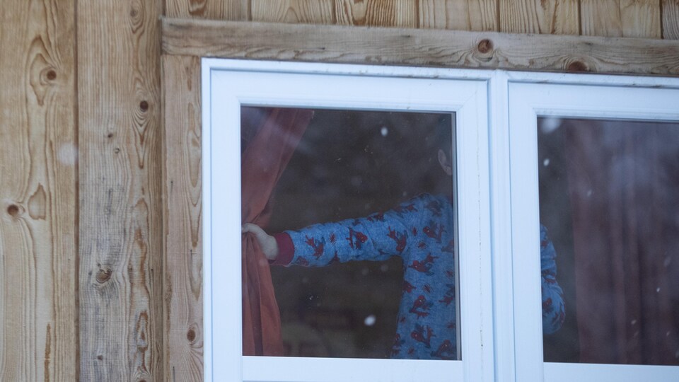 Un enfant en pyjama regarde par la fenêtre.