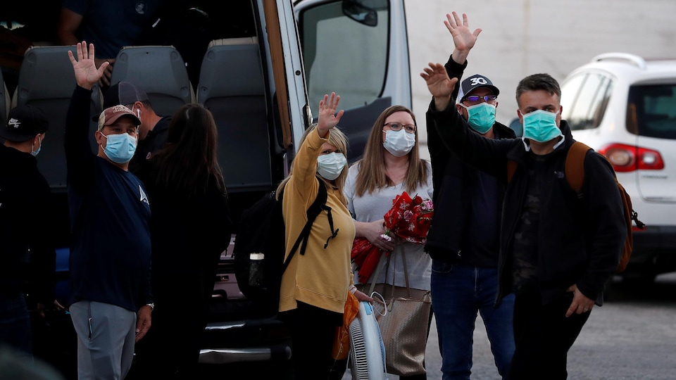 Cinq personnes portant des masques médicaux lèvent les bras pour saluer.