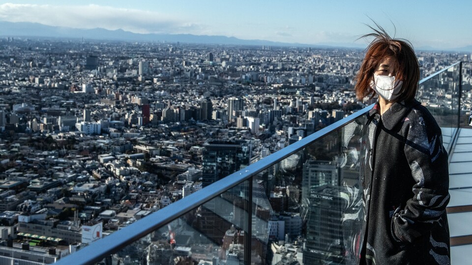 Une femme masquée surplombe Tokyo du haut d'une tour.