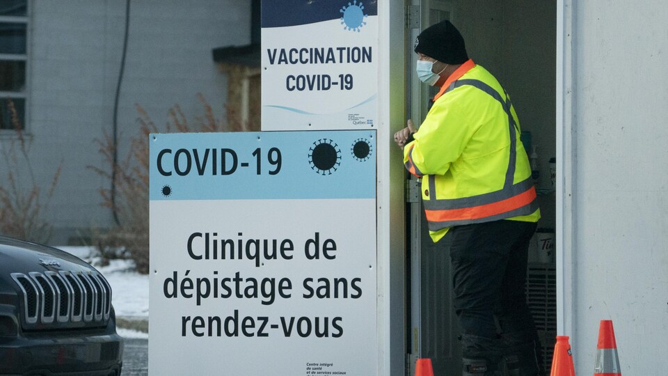 Un préposé attend près d'une affiche qui indique l'emplacement d'une clinique de dépistage.