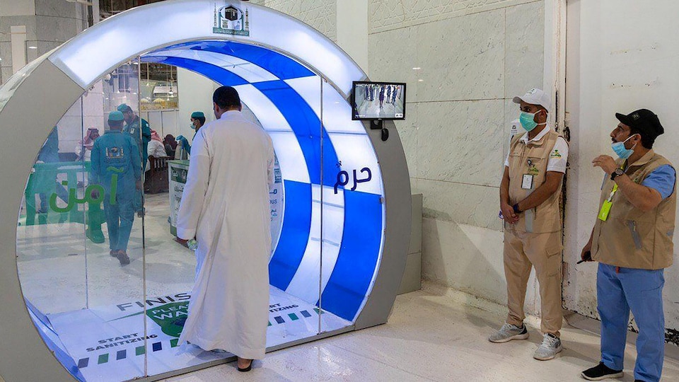 Un homme entre dans un petit espace vitré, sous l'oeil de deux surveillants.