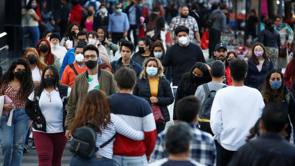 Des gens, certains portant un masque, traversent une rue