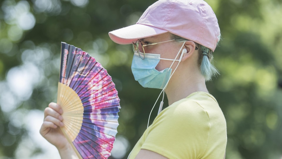 Une femme porte un masque dans un parc et se rafraîchit avec un éventail.