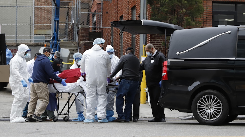 Plusieurs hommes portant des équipements de protection transfèrent le corps dans une voiture.