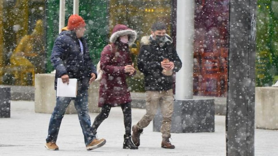 Trois personnes marchent sous des flocons de neige. 