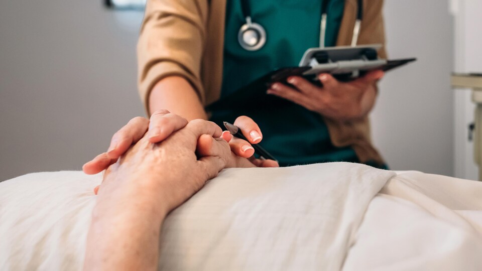 Un médecin tient la main d'une patiente allongée.