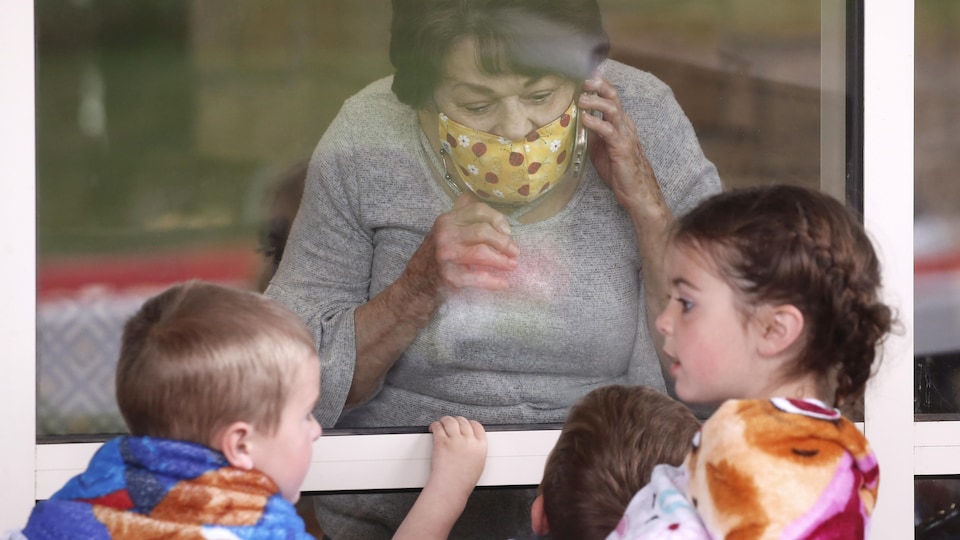 Une femme regarde par la fenêtre ses petits-enfants. 
