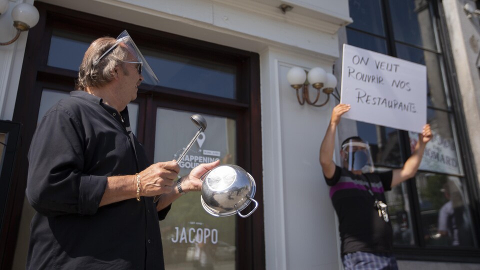 Un homme tient une casserole et un autre une pancarte durant une manifestation.