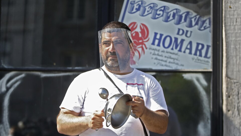 Un homme portant une visière tient dans ses mains une casserole et une cuillère. 
