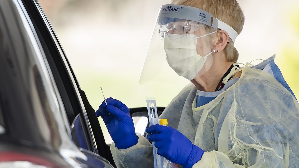 Une travailleuse de la santé tient une tige de test à côté d'un véhicule.