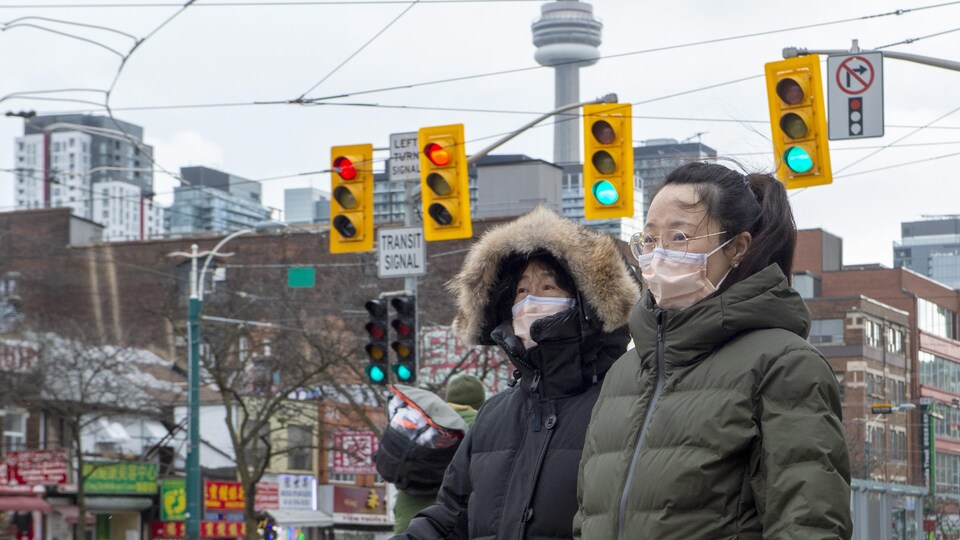 Deux femmes marchent dans le quartier chinois à Toronto en portant un masque.