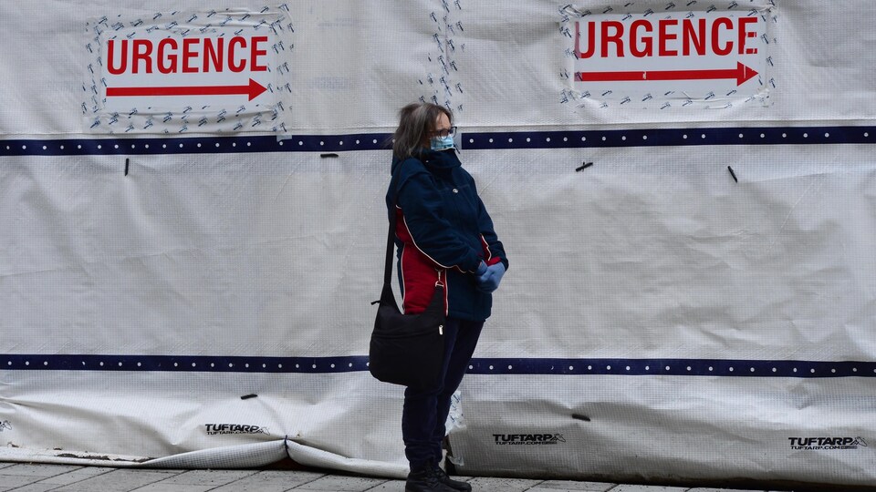 Une femme attend debout près d'indications indiquant la direction à suivre pour accéder à l'urgence.