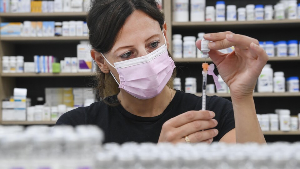 Une pharmacienne pousse une seringue dans une fiole.