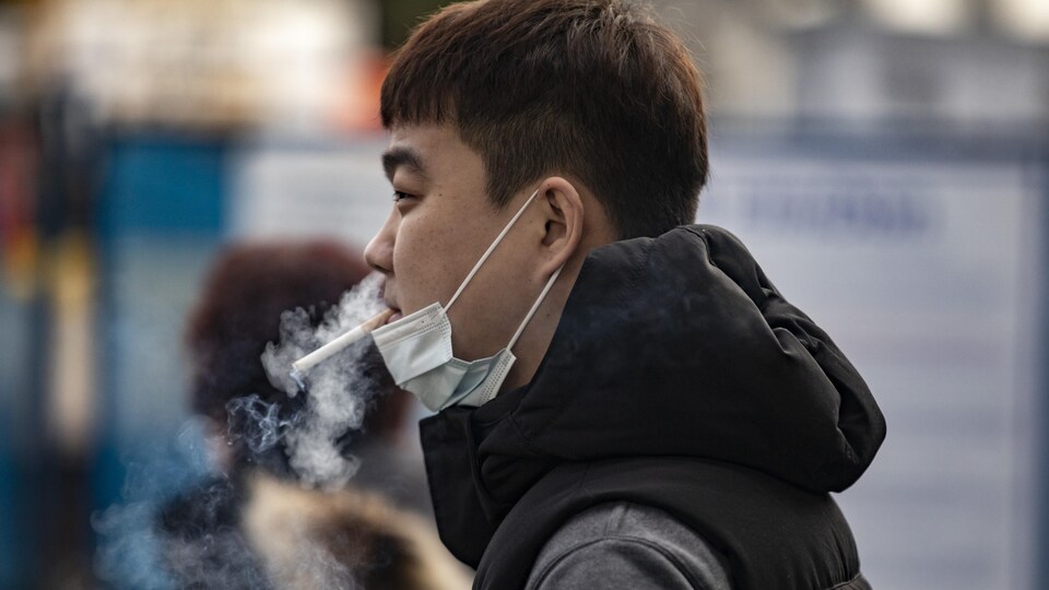 Un homme porte un masque et fume une cigarette.