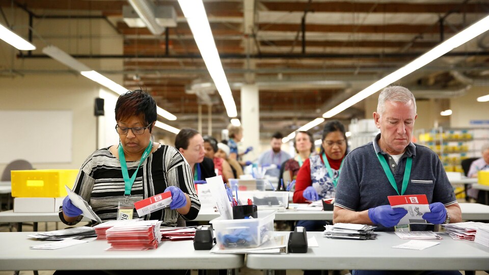 Des travailleurs électoraux, portant des gants, ouvrent les enveloppes contenant les bulletins de vote avant qu'ils ne soient numérisés.
