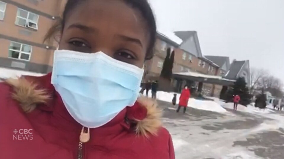 Une femme portant un masque chirurgical est dehors, et d'autres personnes sont dehors derrière elle.