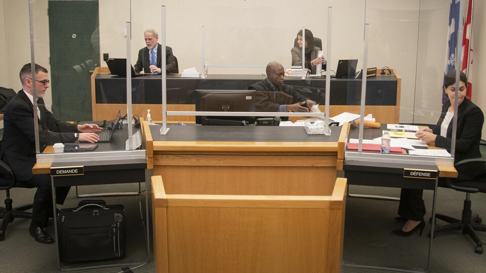 Cinq personnes assises dans une salle d'audience.
