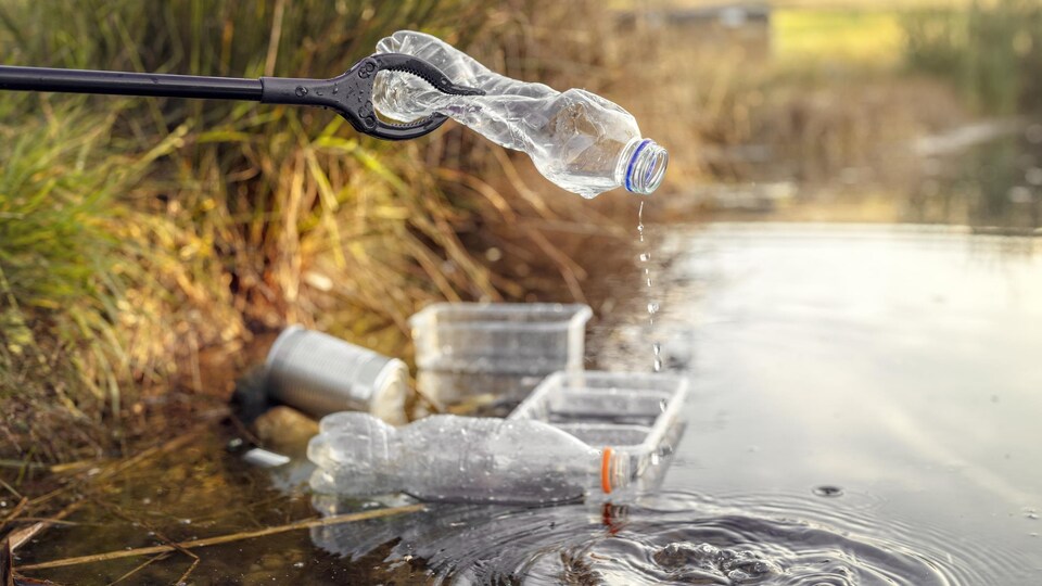 Une bouteille en plastique au bout d'une pince, sur une berge.