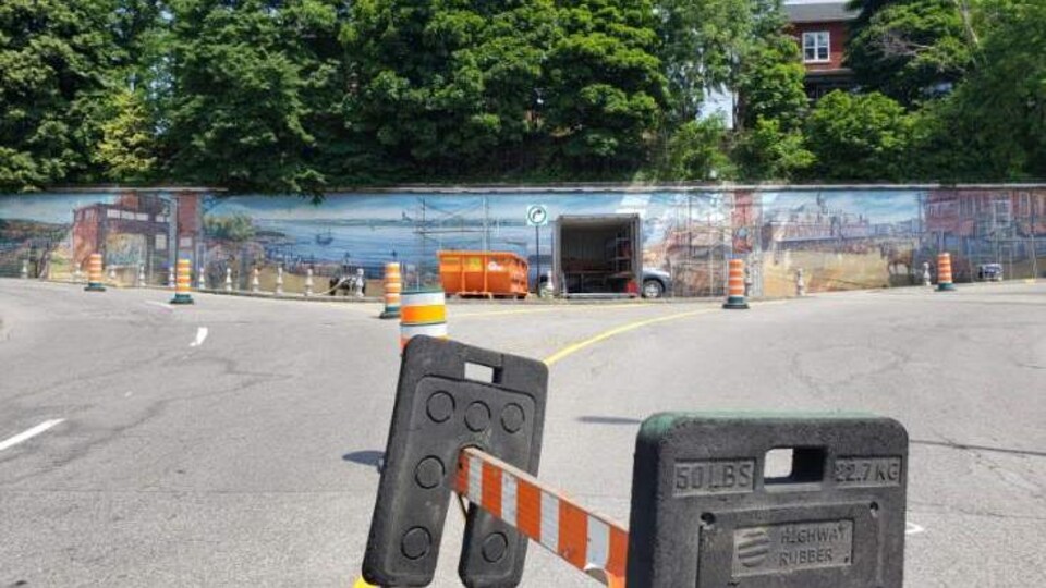 Une énorme murale sur un mur de béton dans la côte Plouffe à Trois-Rivières. En avant-plan, une barricade pour empêcher les gens d'y aller.