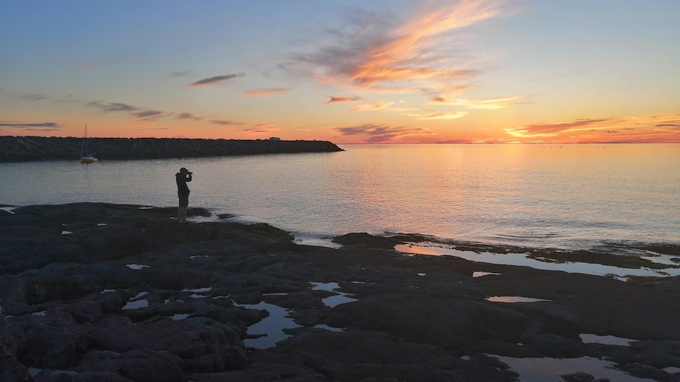 Un homme photographie le coucher du soleil à Rimouski.
