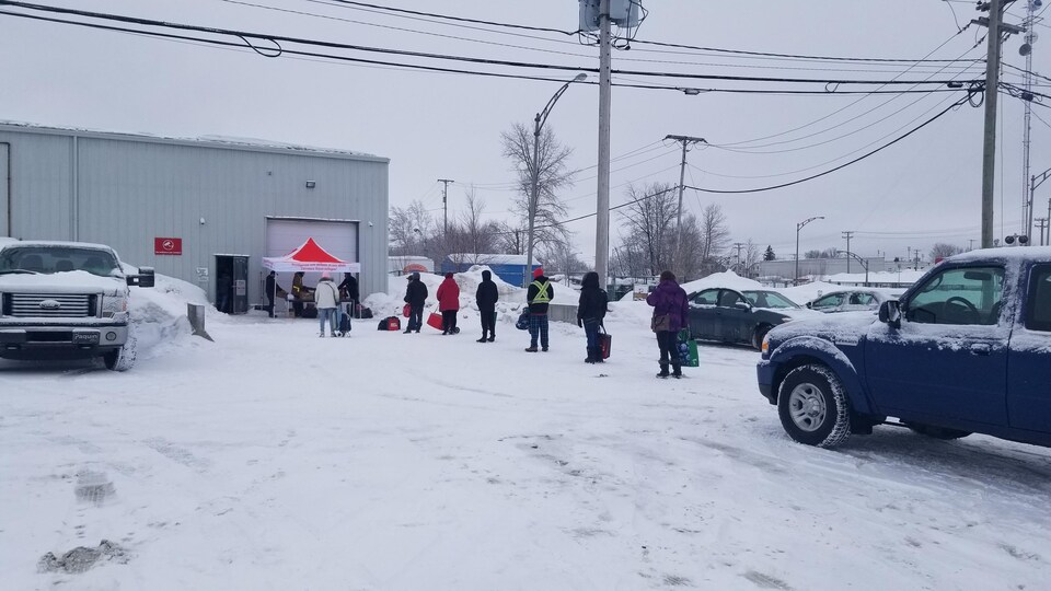 Des personnes font la file pour recevoir de la nourriture dans le stationnement d'une banque alimentaire.