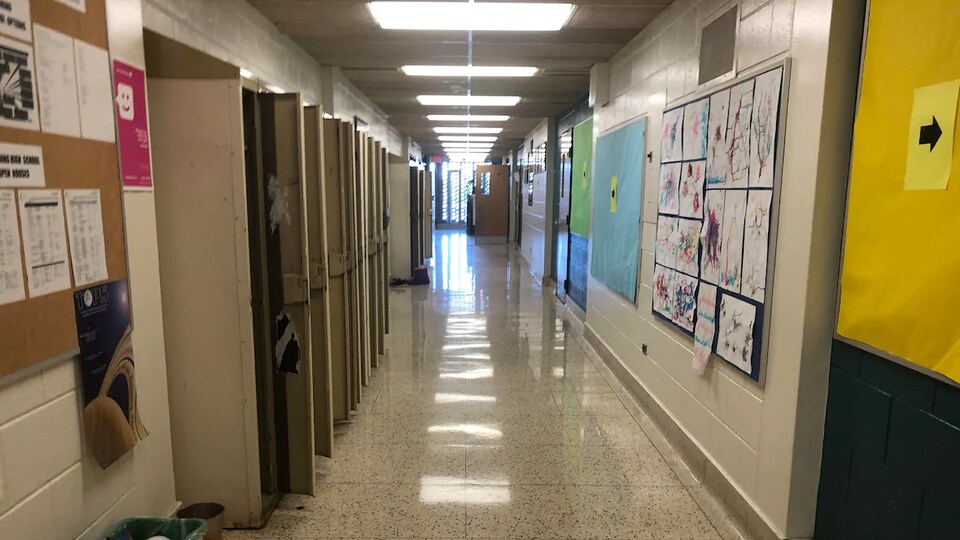 Un corridor vide dans une école. À gauche se trouvent des casiers et à droit des dessins sont affichés sur le mur.
