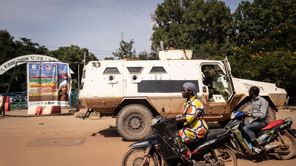 Des personnes en moto qui passent devant un véhicule militaire.