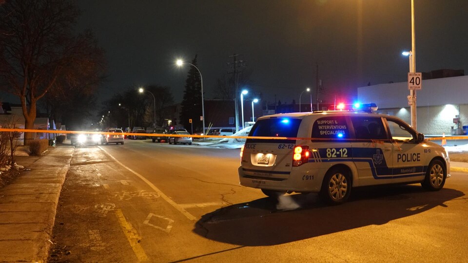 Un véhicule de police dans une rue de Montréal, phares allumés, derrière un ruban policier.