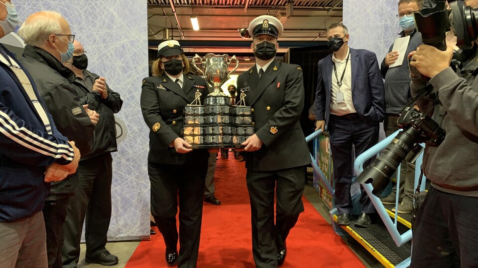 La Coupe Memorial arrive à St-Jean. Des policiers transportent la Coupe, devant une foule de gens.