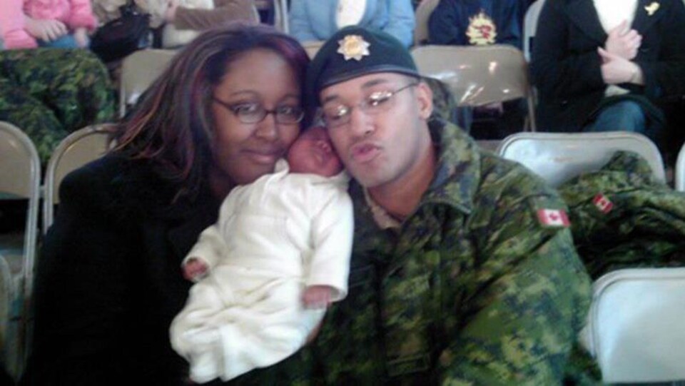 Une femme en civil et un militaire en uniforme posent pour une photo en tenant un petit bébé.