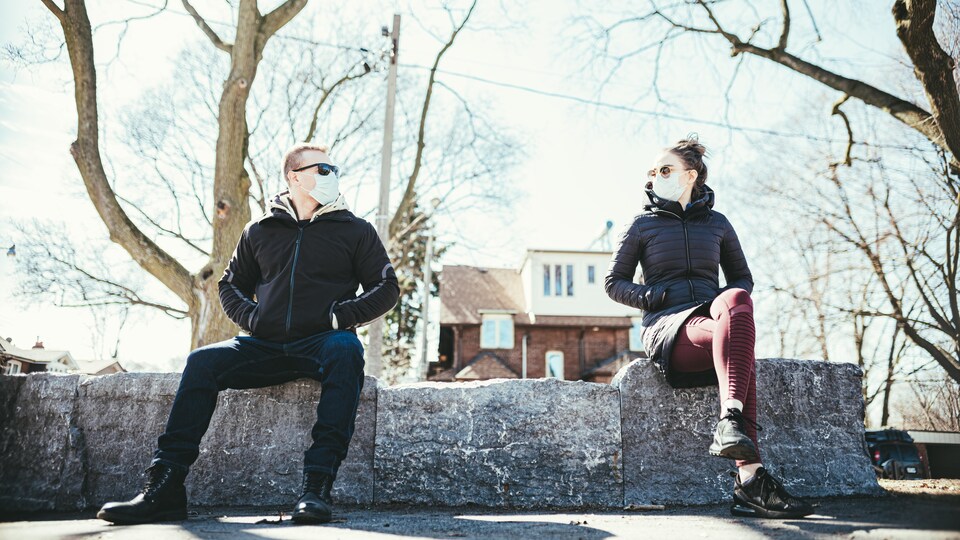 Un couple masqué assis dans un parc à un mètre de distance.