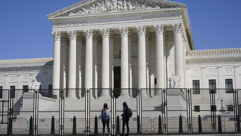 Deux jeunes femmes observent la façade de la Cour suprême des États-Unis à Washington, à l'extérieur des clôtures érigées par mesure de sécurité.