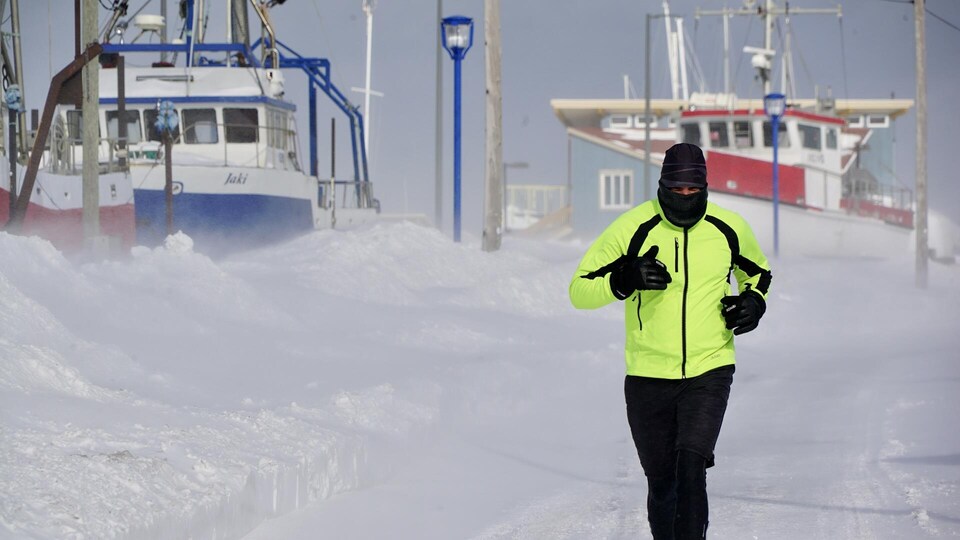 Un homme court à l'extérieur, près d'un quai de bateaux en plein hiver.