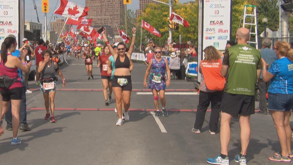 Une coureuse lève les bras en l'air, fière d'avoir achevé la course. Des drapeau du Canada flottent derrière elle.