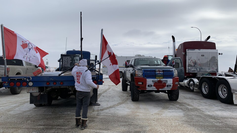 Un manifestant tient un drapeau du Canada devant des camions stationnés près de voitures de police.