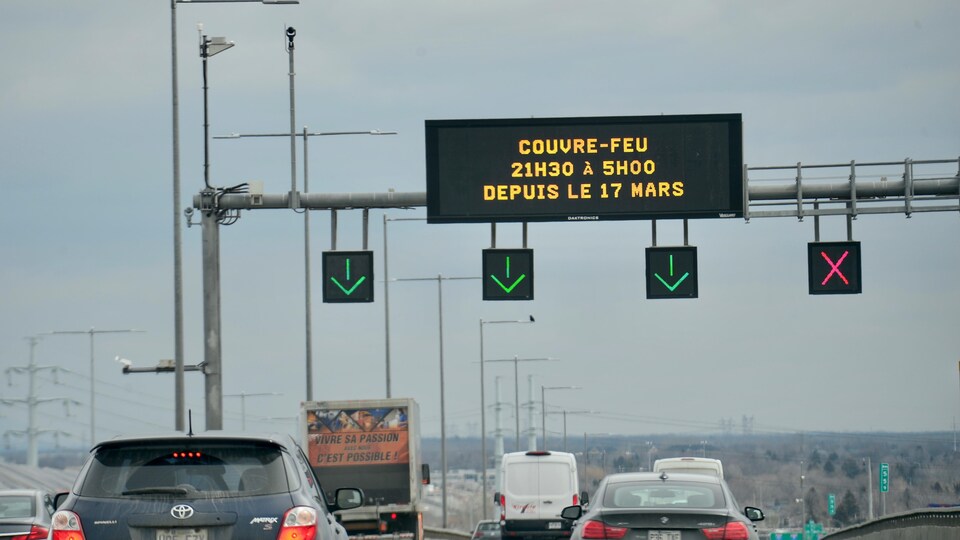 Des voitures passent sur l'autoroute avec un panneau annonçant l'heure du couvre-feu.