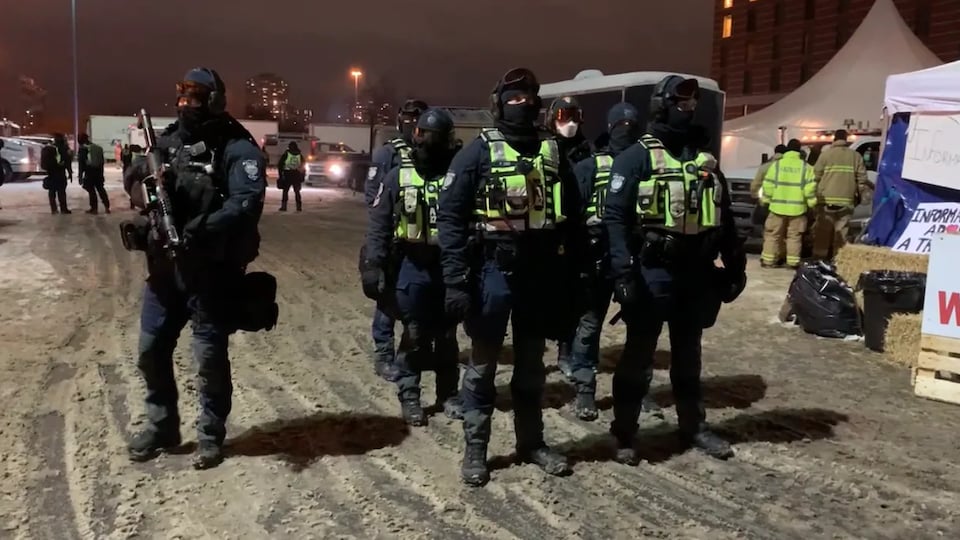 Des policiers avec des armes et des gilets pare-balles dehors, lors d'une intervention en hiver dans un camp.