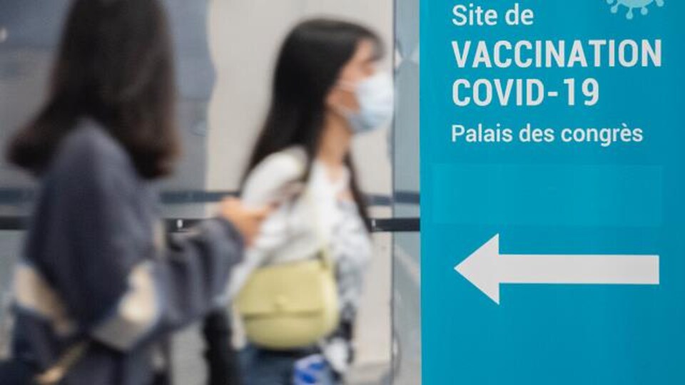 Des personnes portant un masque marchent vers un centre de vaccination.