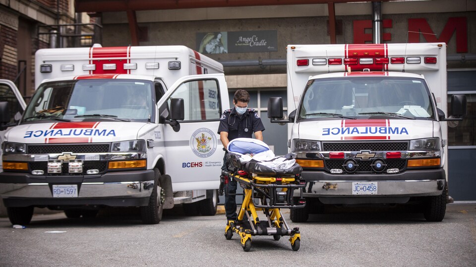 Un ambulancier pousse une civière entre deux ambulances à l'hôpital St-Paul de Vancouver.